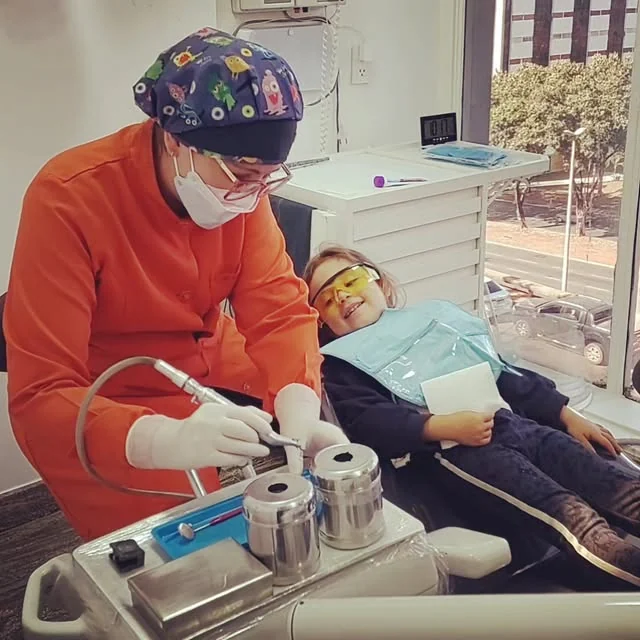 Dentista da CORP atendendo uma criança com óculos de proteção na cadeira